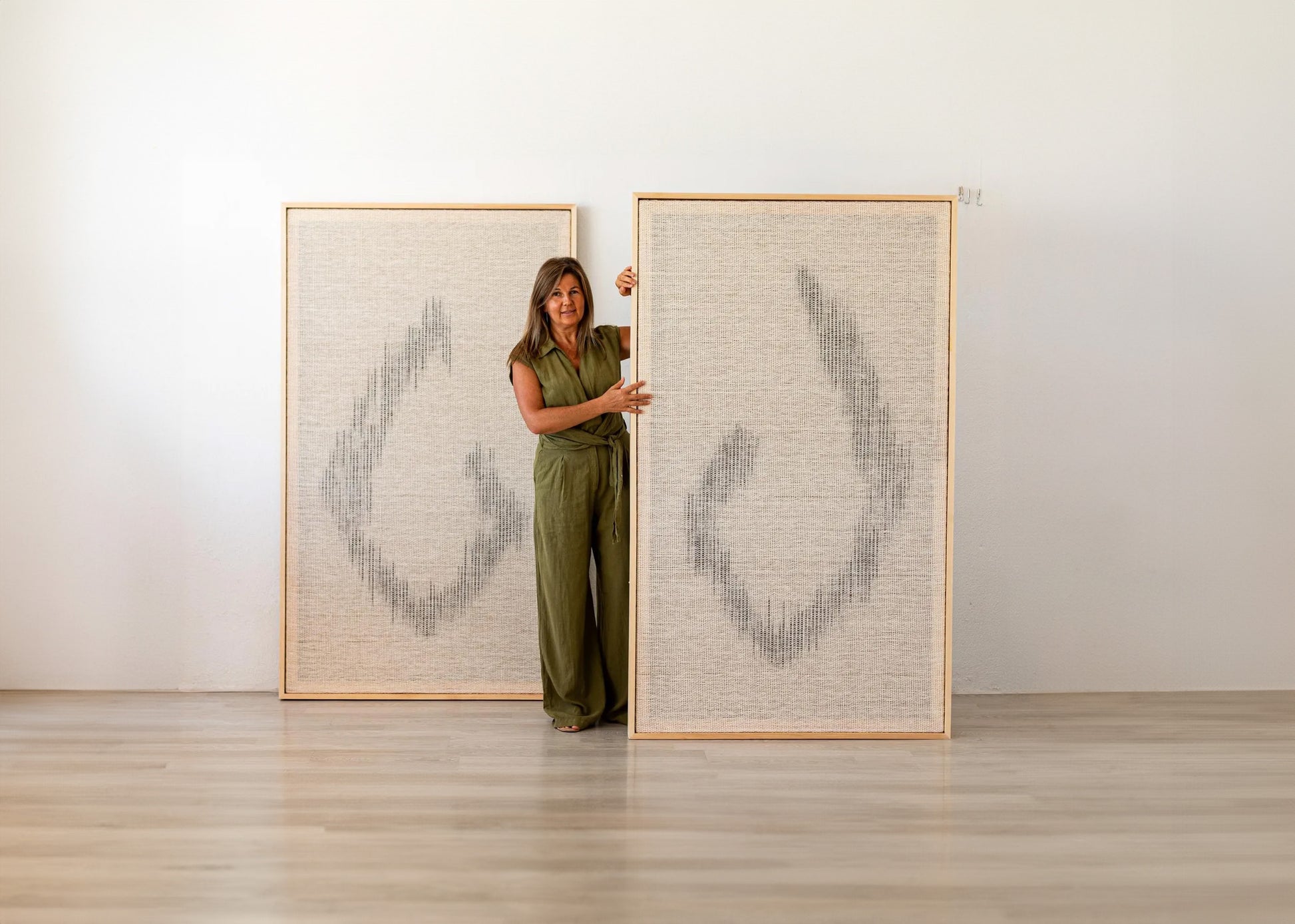 Large handwoven wool tapestries with abstract patterns in natural tones, displayed with a woman standing between them for scale.