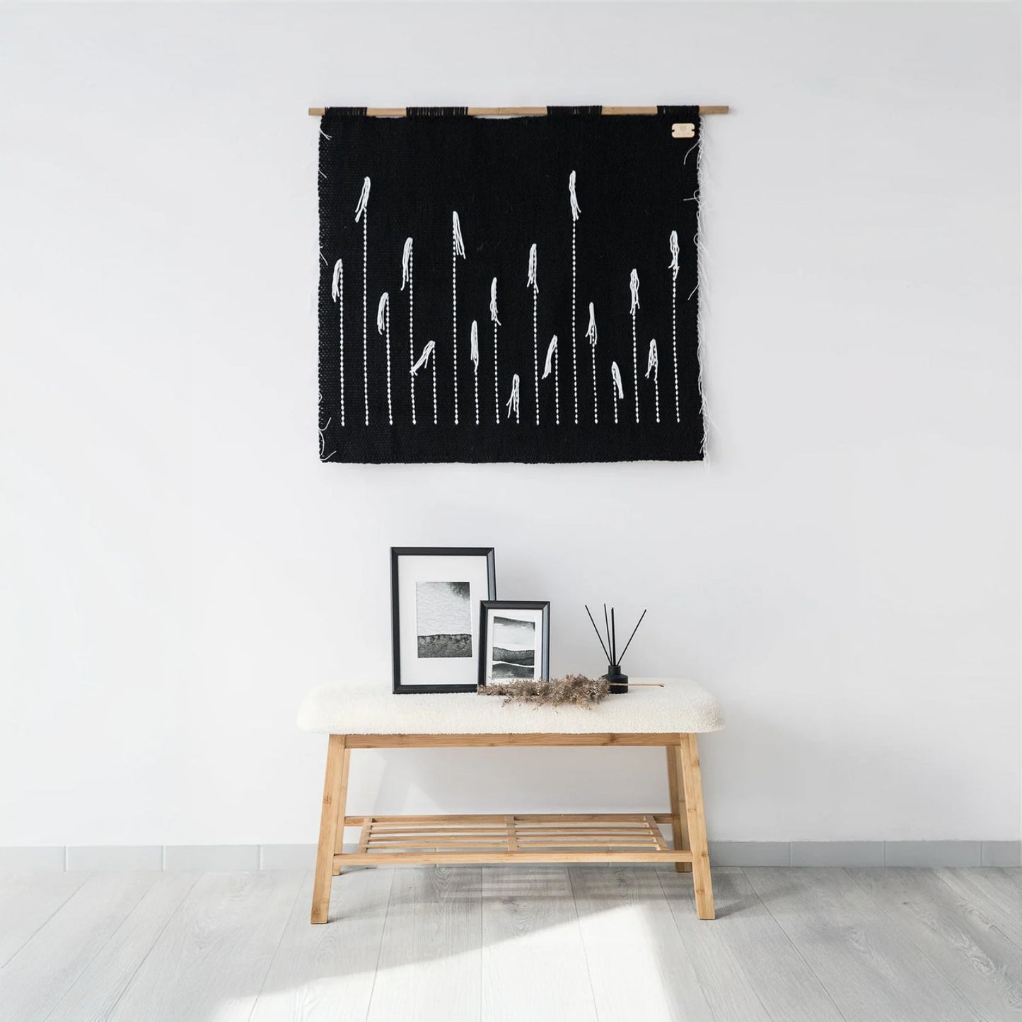 Handwoven black tapestry with white dandelion-inspired design, suspended on a bamboo rod, perfect for modern and minimalist interiors.