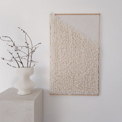 Framed handwoven tapestry with a textured loop design in neutral tones, displayed next to a minimalist white vase, perfect for modern and artistic interiors.