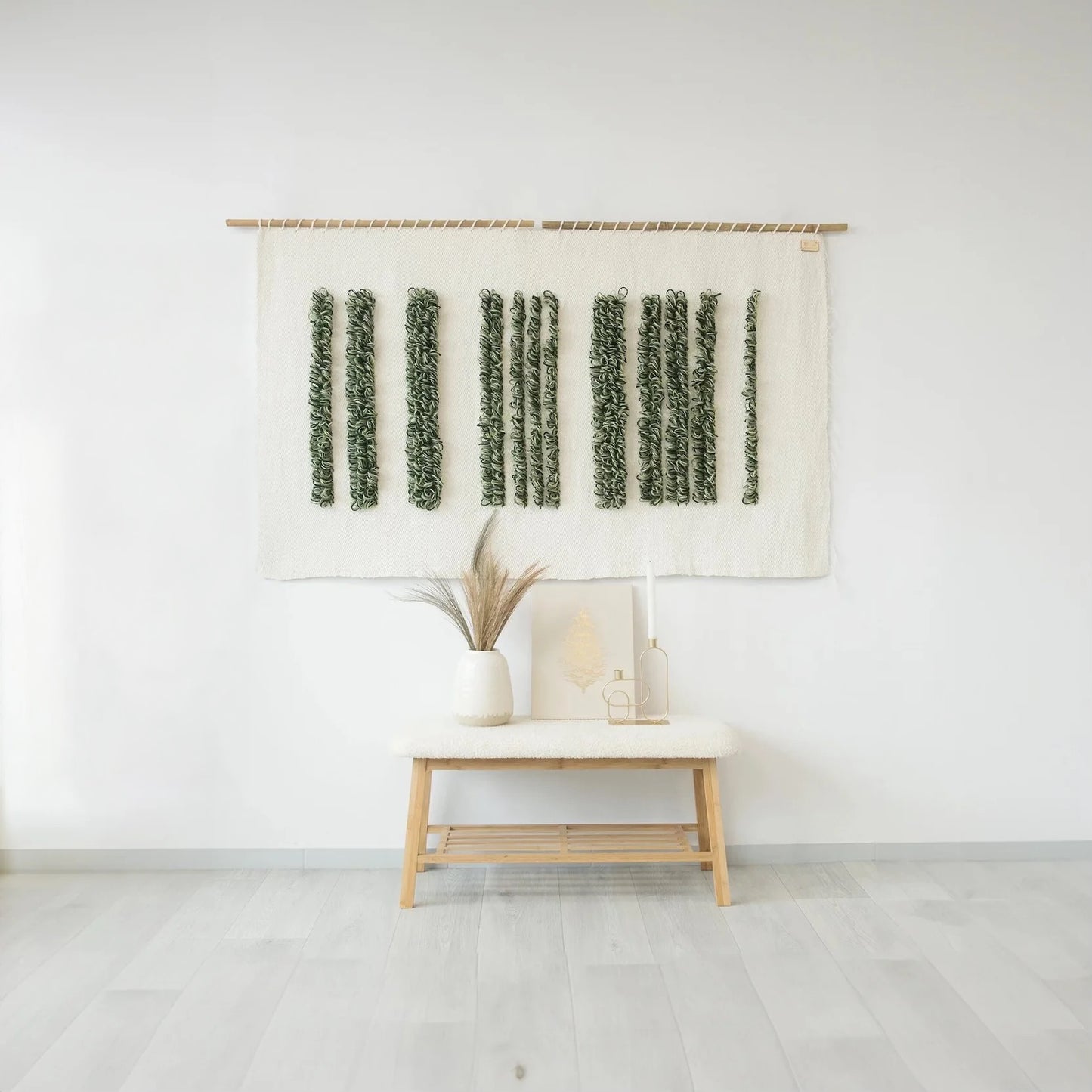 Handwoven Green Luna wall tapestry with vertical green loops on a raw white wool background, hung on a bamboo rod, styled in a modern minimalist interior with natural decor elements.