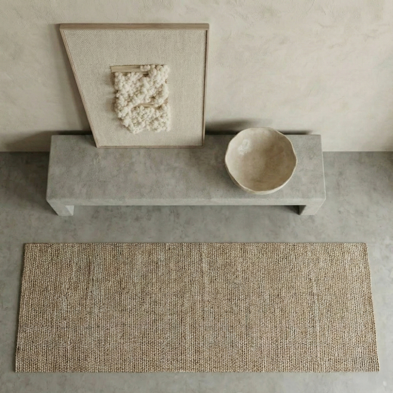 Beige woven rug on a concrete floor with a stone bench and bowl in the background.