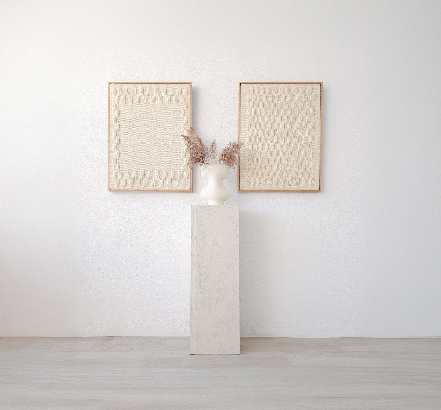 Set of two handcrafted minimalist wall hangings in neutral tones, framed in natural wood, displayed with a modern vase on a pedestal.