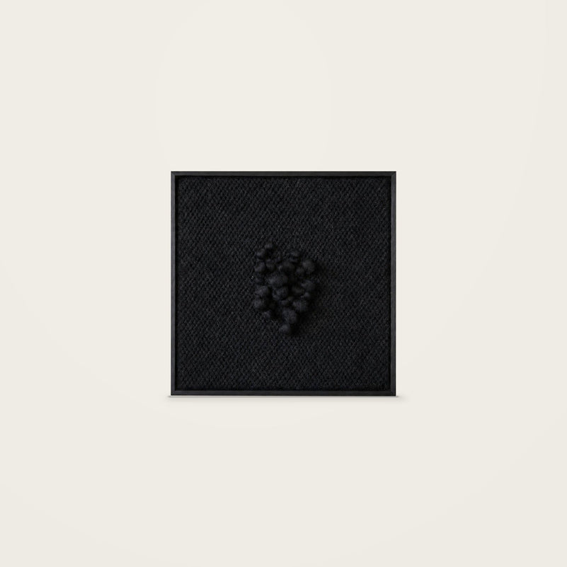 Enigma — black handwoven wool tapestry with raised central texture in a black wooden frame, front view.