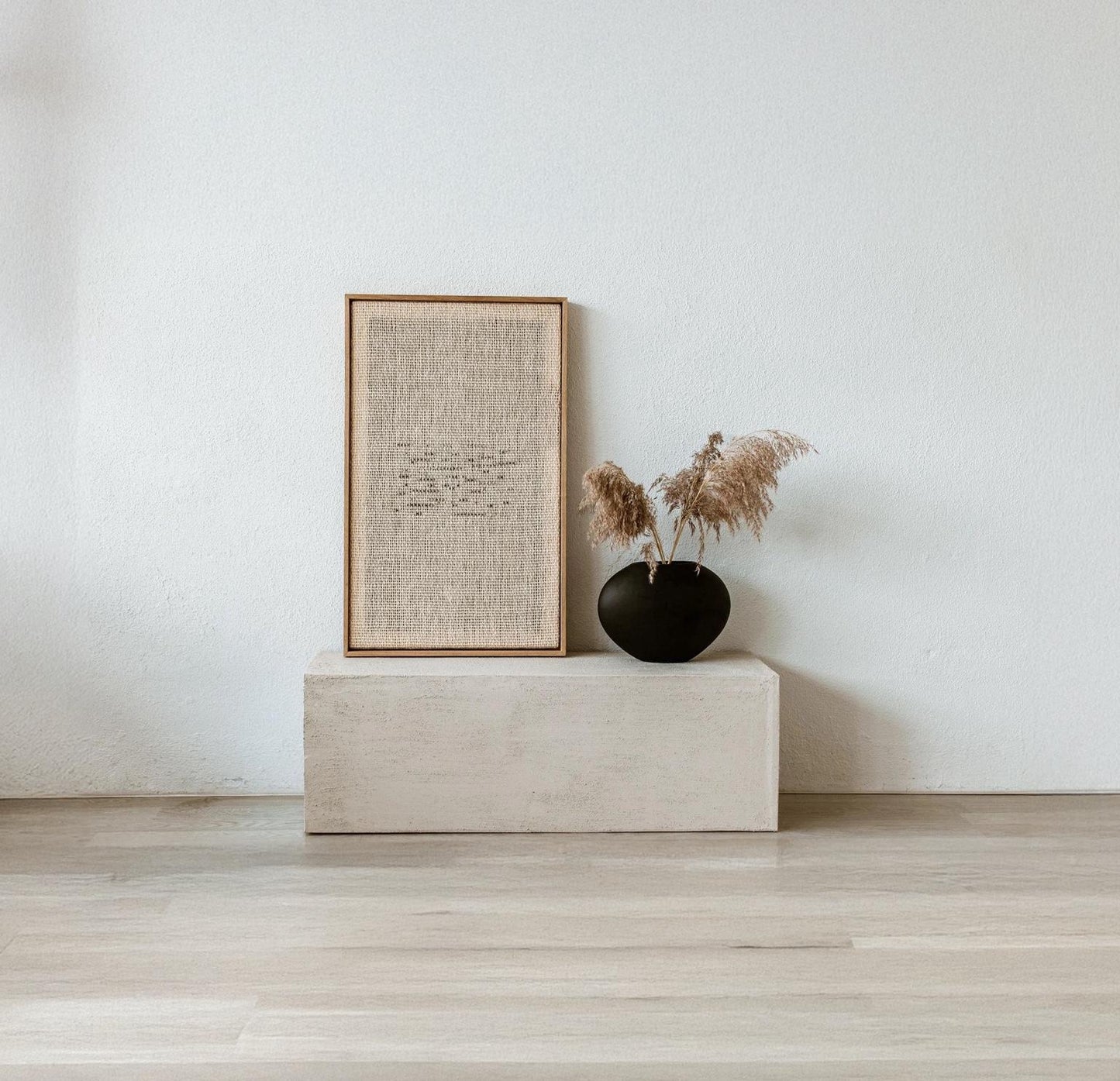 Framed handwoven tapestry in neutral tones, displayed with a black vase and pampas grass, perfect for minimalist and natural decor.