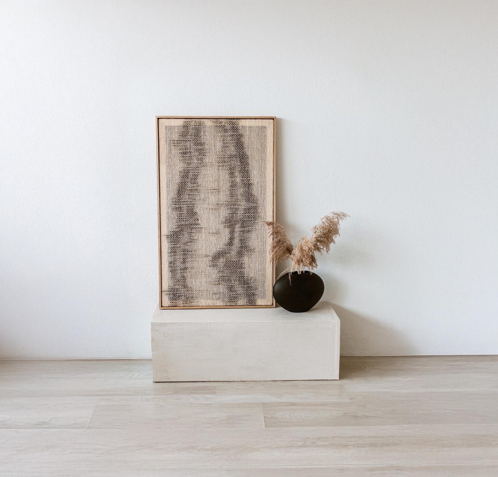 Framed handwoven tapestry with abstract gray patterns, displayed alongside a black vase with pampas grass, perfect for modern and minimalist interiors.