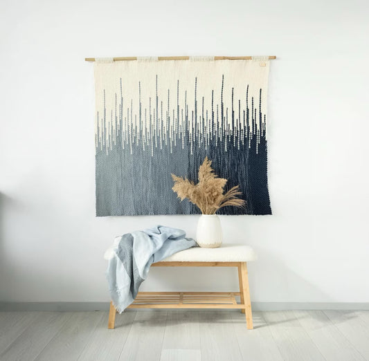 Handwoven Grave wall tapestry with gradient blue tones, crafted from wool and hung on a bamboo rod, displayed in a modern interior with minimalist decor.