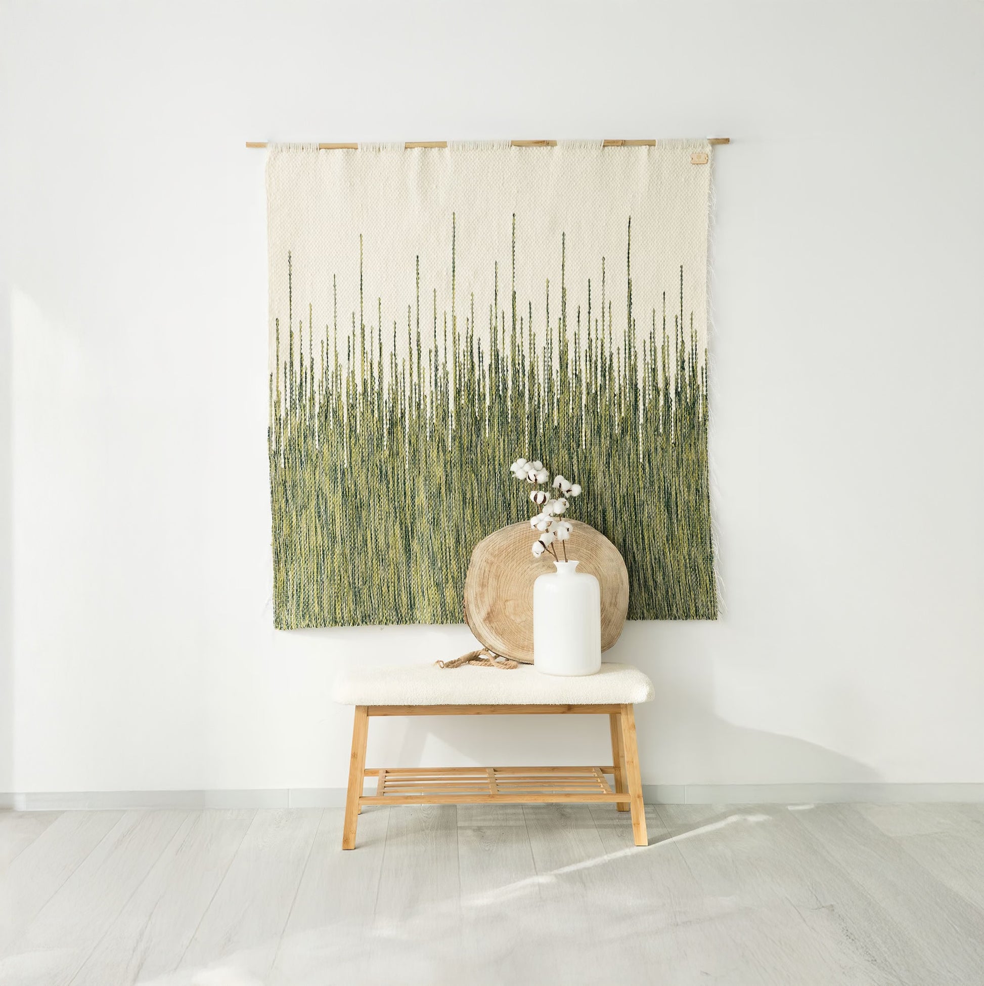 Handwoven wall tapestry in gradient green tones and raw white wool, featuring a zigzag pattern, crafted from wool and hung on a bamboo rod, displayed in a minimalist interior with natural decor elements.