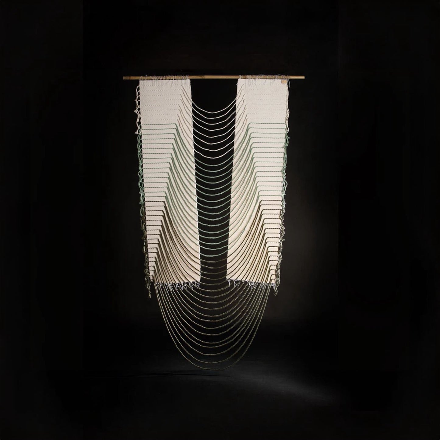 Handwoven neutral-toned wall hanging with symmetrical white cotton panels connected by curved woven threads, suspended on a bamboo rod, displayed on a sleek black background for a modern and minimalist aesthetic.