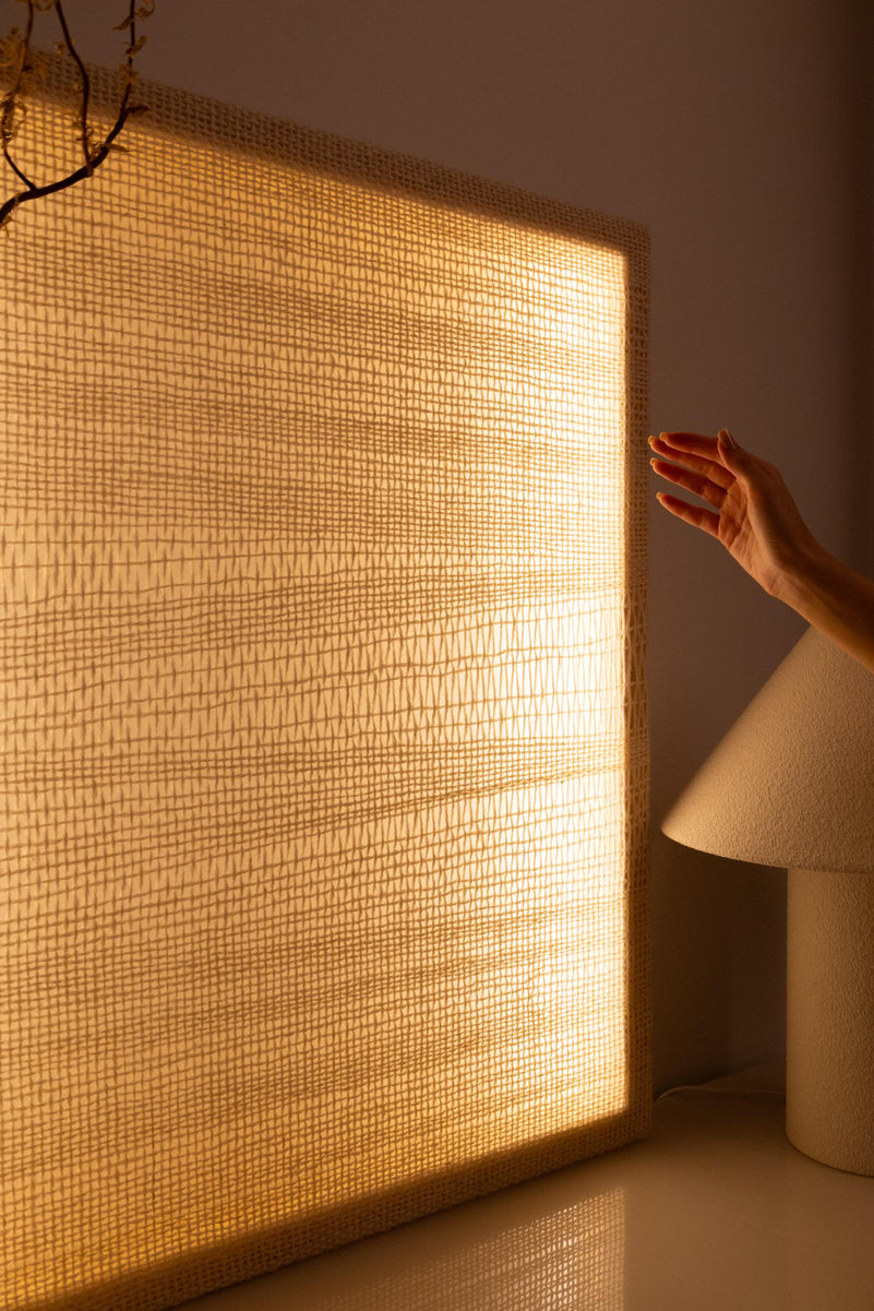A hand beside the illuminated wool tapestry showing the scale, texture and warm ambient light
