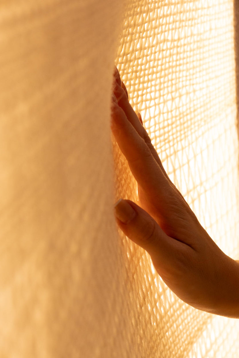 Close view of a hand touching the illuminated raw white wool weave as light passes between the threads