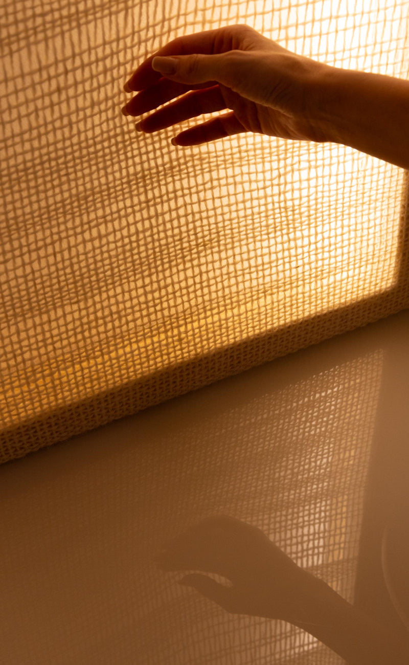 Hand reaching toward the glowing wool tapestry with its woven pattern reflected on the surface below