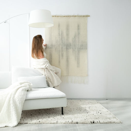 Handwoven Misty wall tapestry crafted from natural wool in neutral tones, perfect for modern and boho-style interiors. Featured in a cozy living room with soft textures, bringing warmth and sophistication to any space.