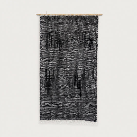 Nyora handwoven two-ply wool tapestry in charcoal and black with a dripping vertical pattern on a slim bamboo rod, minimalist Japandi textile wall art by Lale Studio & Shop