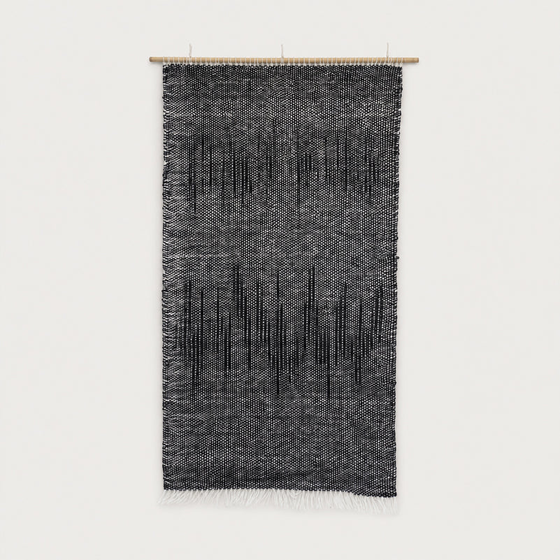 Nyora handwoven two-ply wool tapestry in charcoal and black with a dripping vertical pattern on a slim bamboo rod, minimalist Japandi textile wall art by Lale Studio & Shop