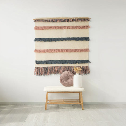 Pipi handwoven wool tapestry featuring soft natural tones, blue, and powder pink fringes. Elegantly displayed on a wooden rod, this artistic wall hanging adds texture and warmth to any modern or boho-inspired interior.