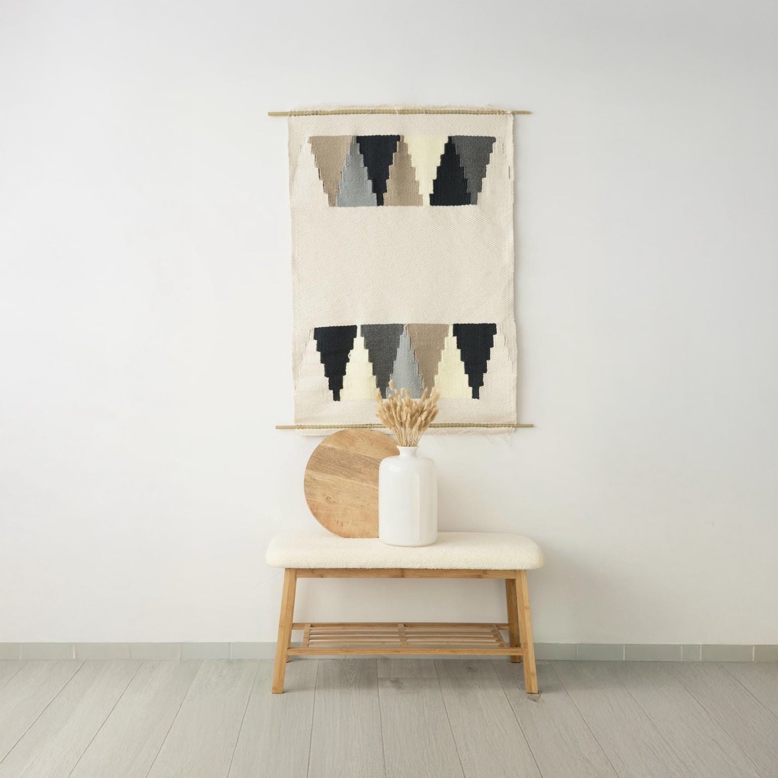 Triangul handwoven wall tapestry featuring a modern geometric triangle design in natural wool tones of beige, black, and gray, suspended on a bamboo rod. Perfect for elevating boho or modern interiors with luxurious decor.